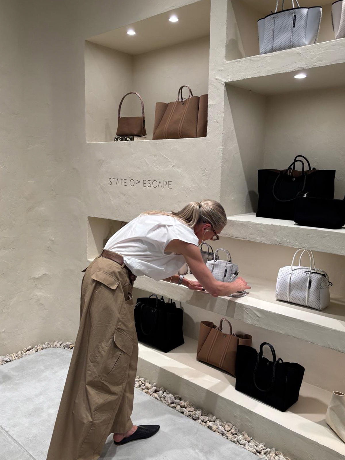 Person arranging bags on shelves in a boutique display.