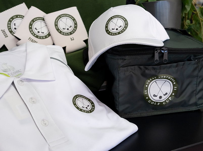 Merch collection for Great Northern Golf Cup featuring white structured cap, personalised name white stubby holders, polo and cooler bag, all with the same DTF circular logo. 