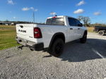 Rear view of white RAM 1500 with black tailgate lettering and trailer hitch on gravel