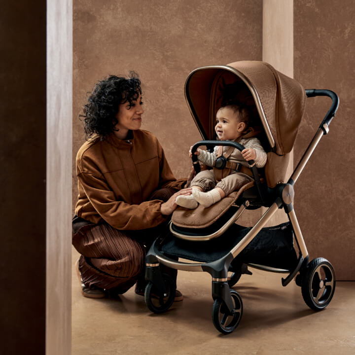 A woman interacts with a smiling baby in a stroller indoors.