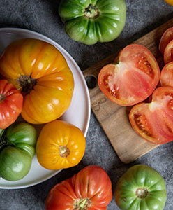 Assorted heirloom tomatoes in various colors on a dark surface.