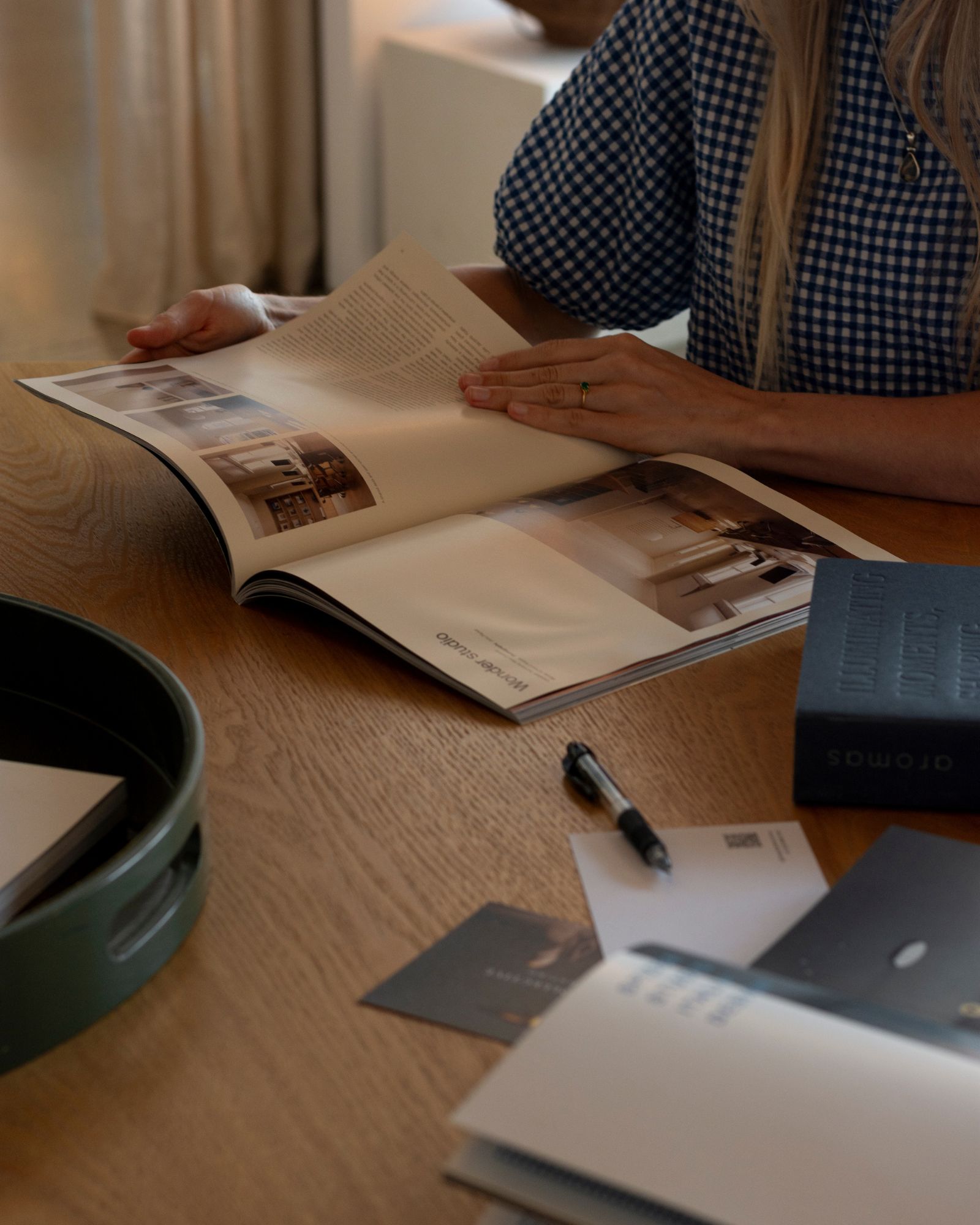 Person flipping through a magazine on a wooden table with stationery.