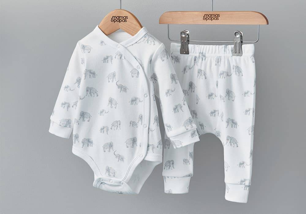 A white baby grow and leggings with an elephant print hang on a wooden rail.