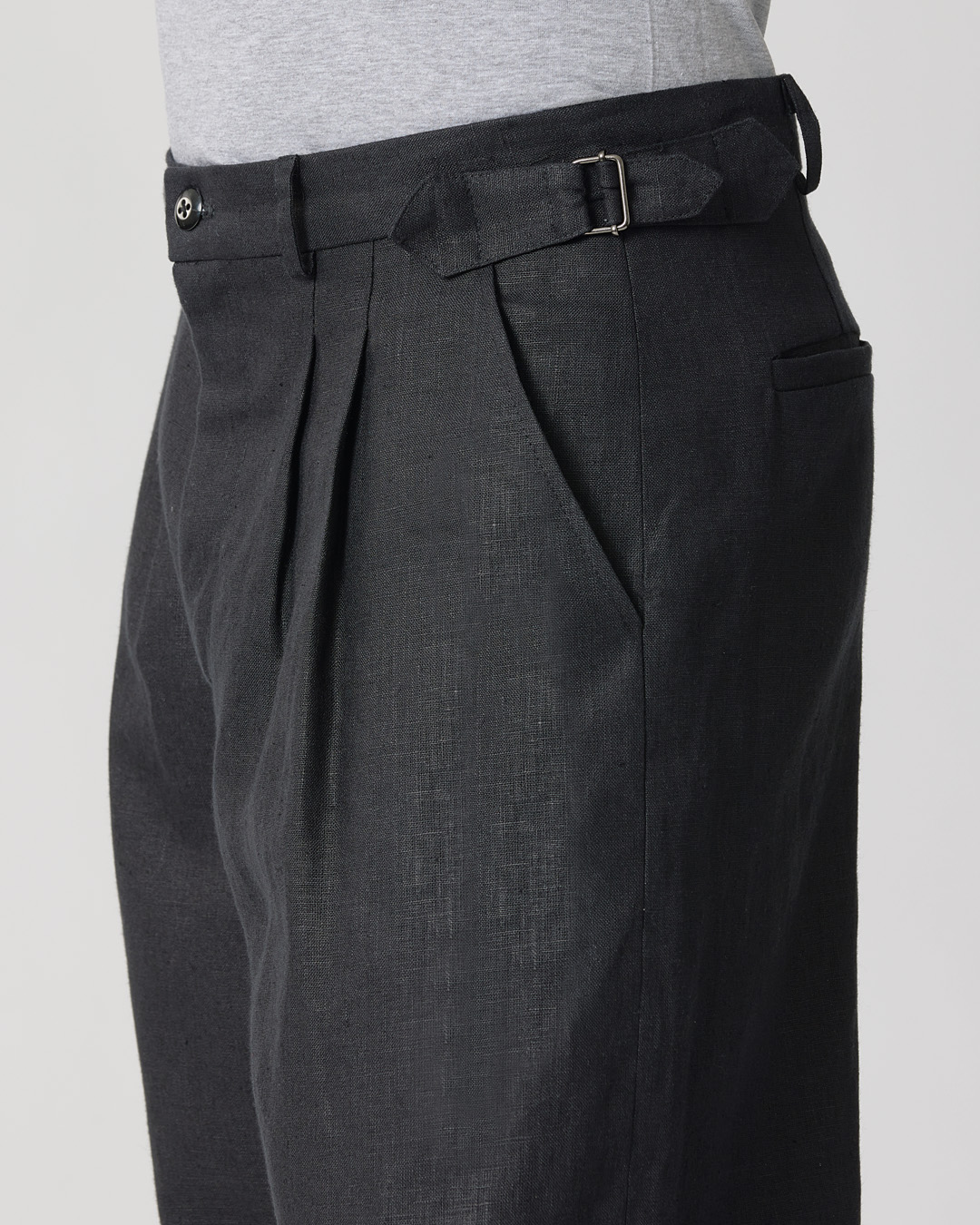 Side view of black pleated trousers with a belt.