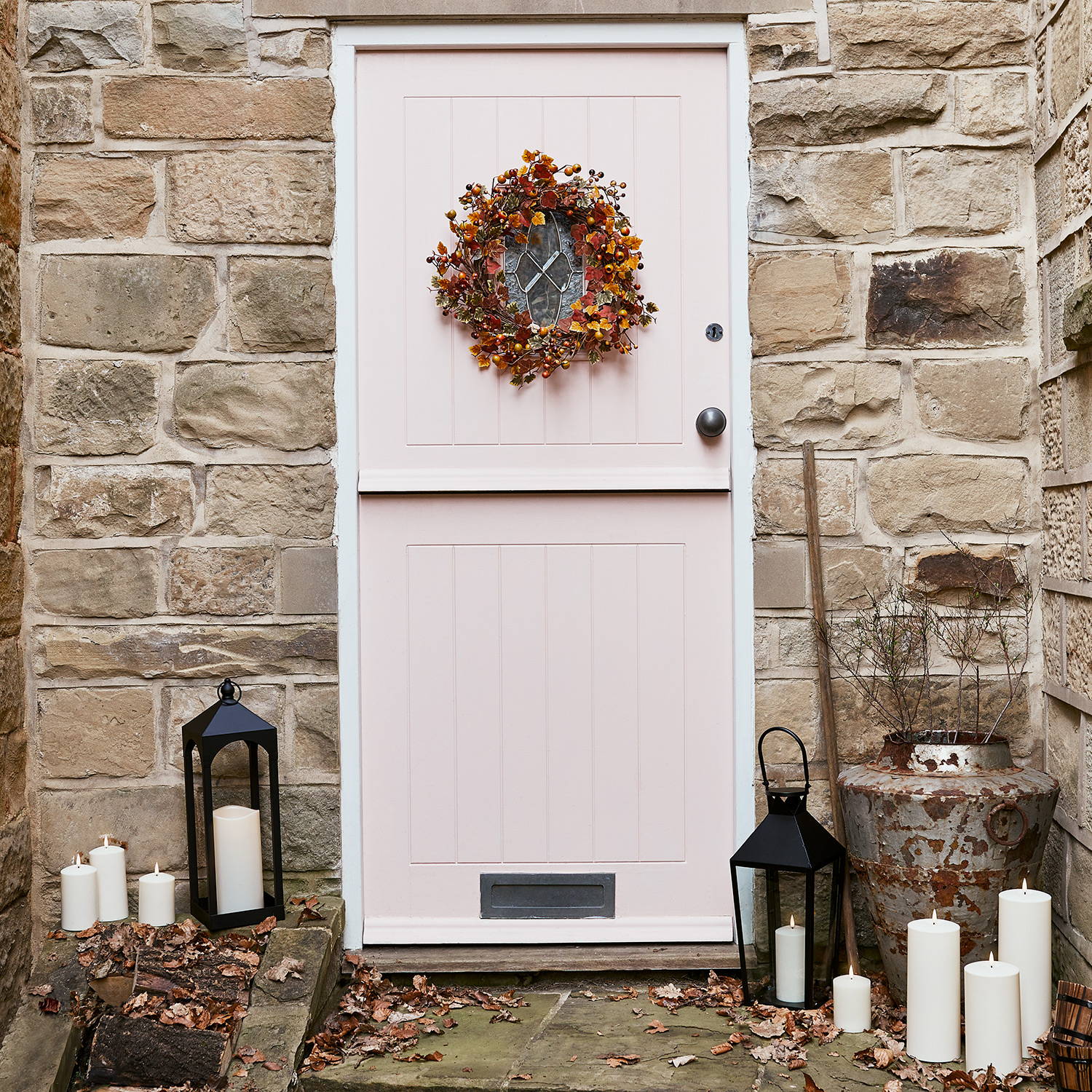 An autumn entrance with a pink door, autumn wreath, LED outdoor candles and black lanterns.