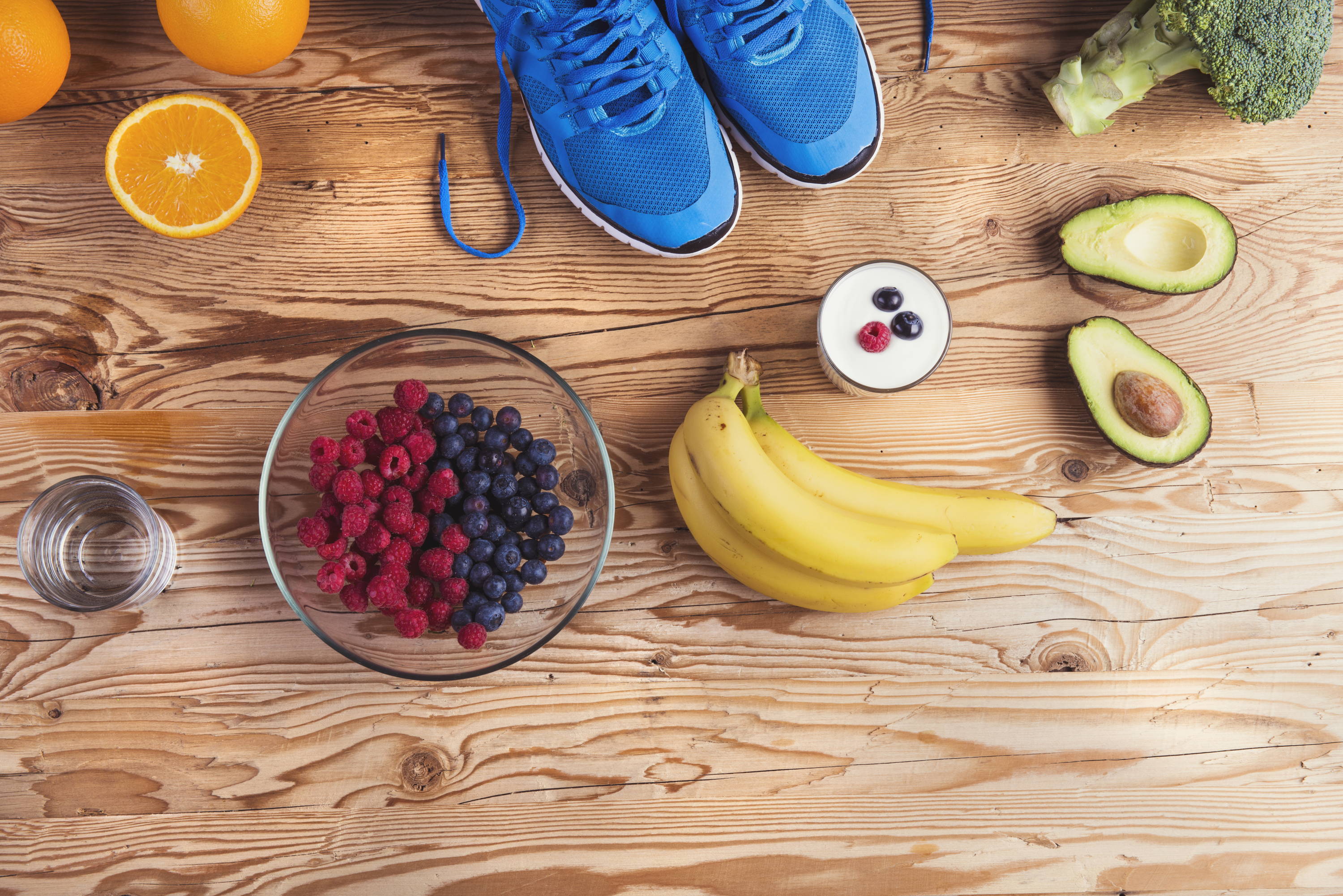 Bananas, avocado, yogurt, berries, water and oranges on a table 