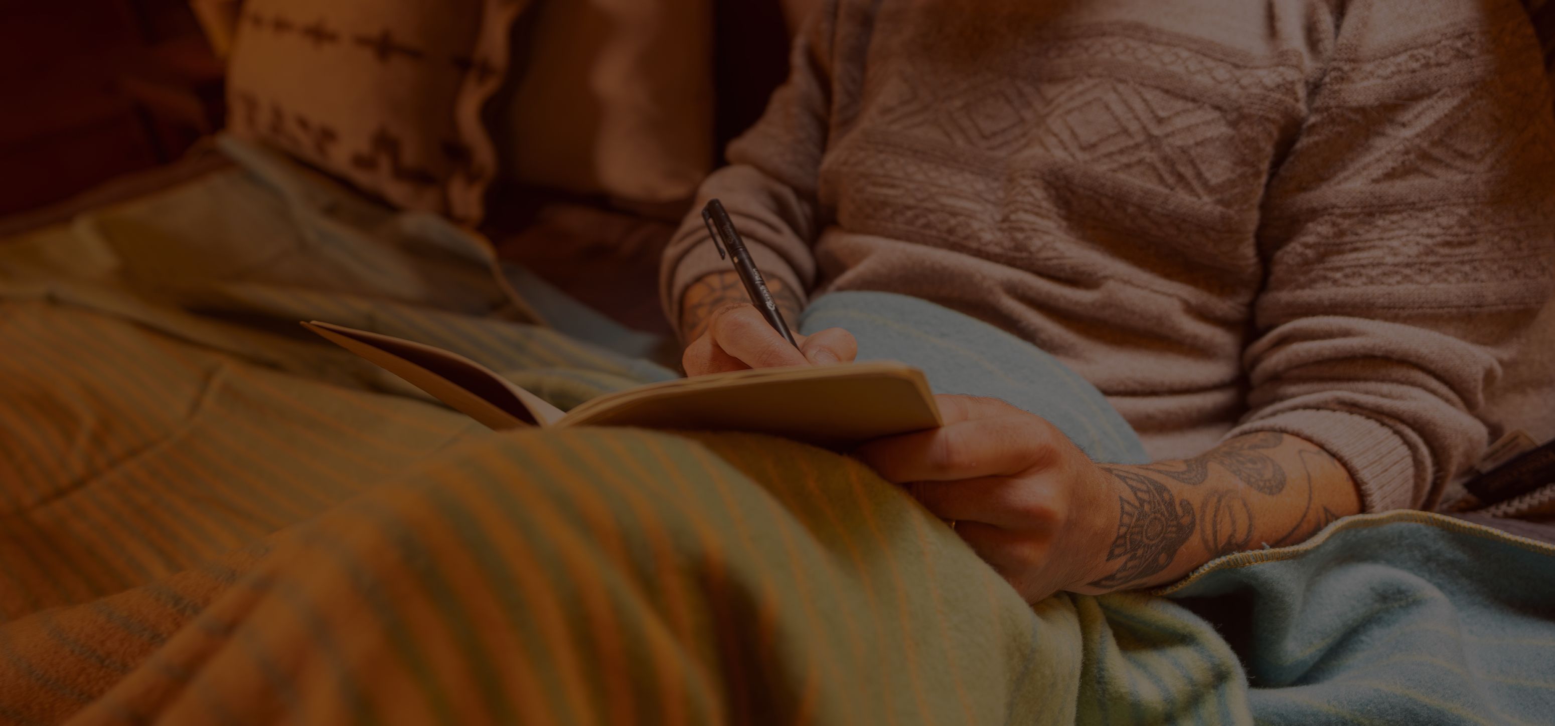 Person reading a book while seated on a bed.