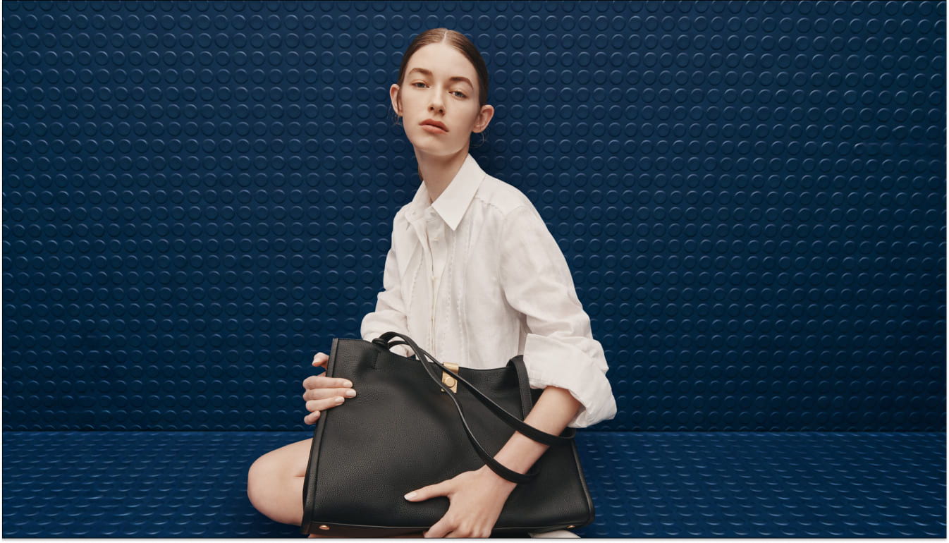 Model in white shirt with a black handbag against a blue background.