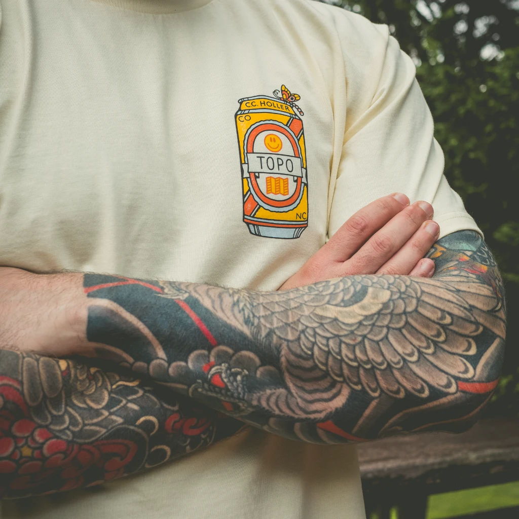 Arm with detailed tattoos and a shirt featuring a beverage design.