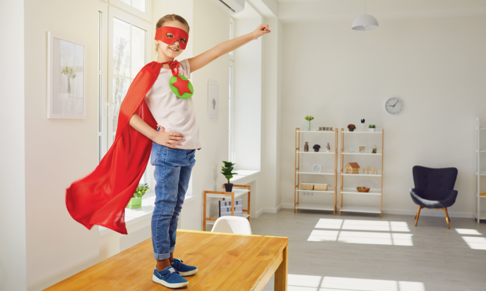 Child in a superhero costume standing triumphantly on a table.
