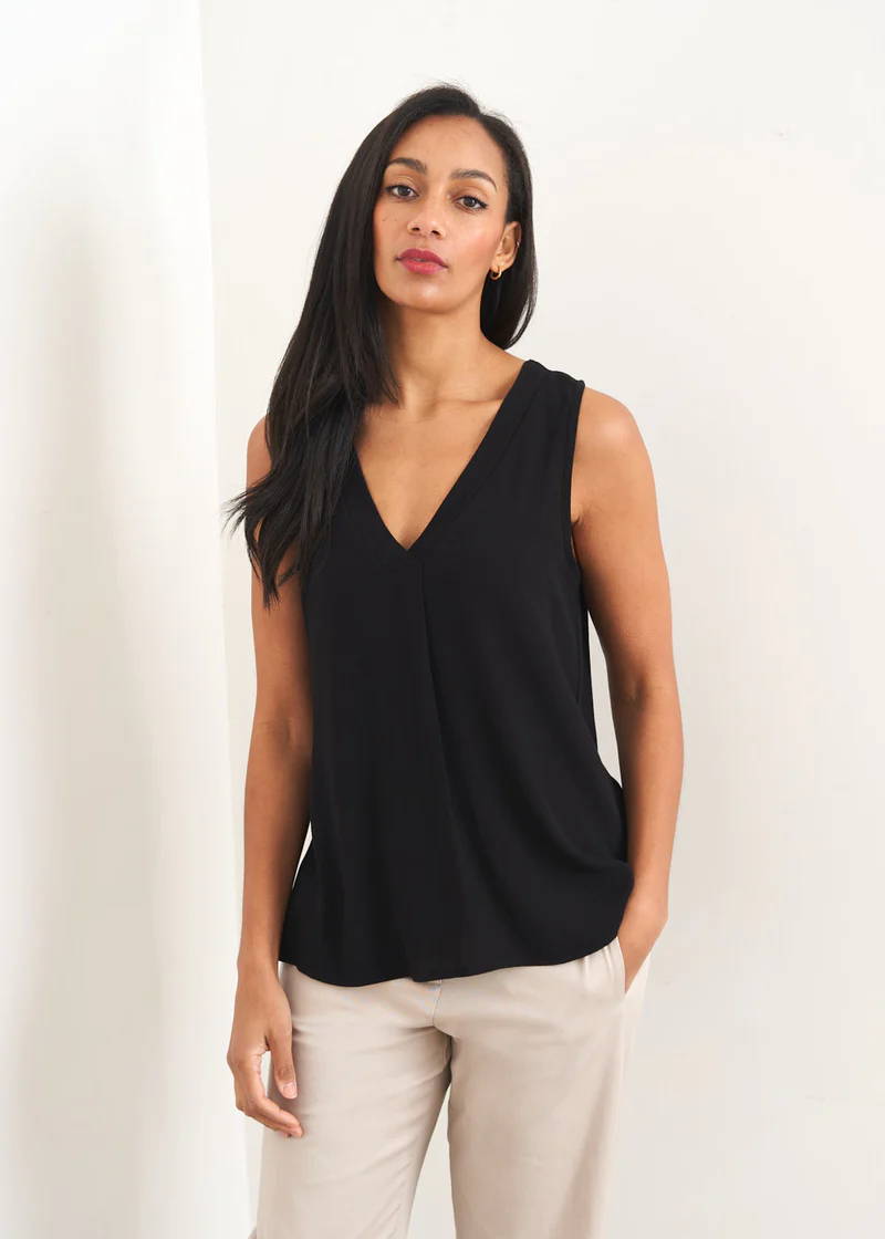 A model wearing a black sleevless vest with a v neckline and off whie trousers