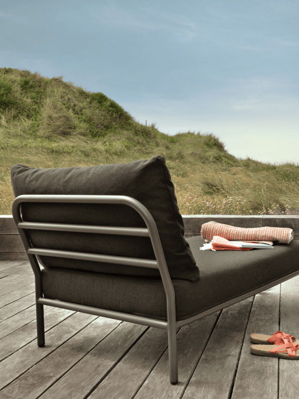Modern outdoor lounge chair with dark cushions and a powder-coated metal frame on a weathered wood deck beside a small black side table.