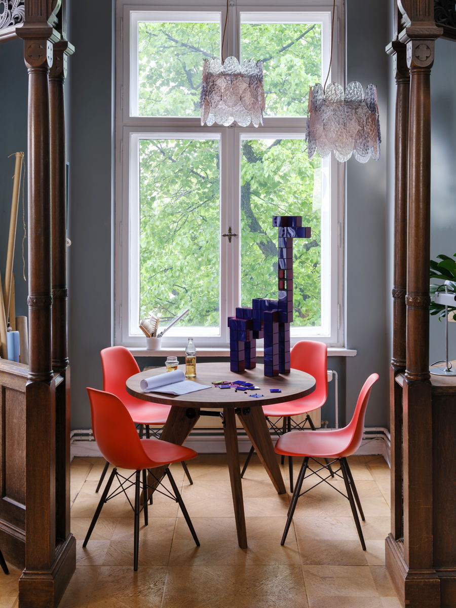 A cozy Vitra dining area with a round table and colourful DSW chairs near a window.