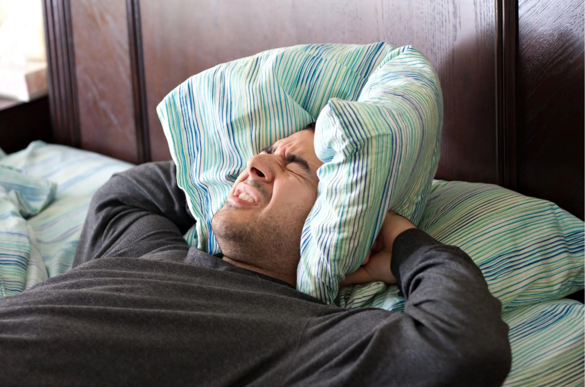 sleepless man with pillow around ears