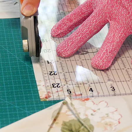 cutting fabrics for quilting with a rotary cutter ad ruler on a cutting mat wearing a pink safety glove
