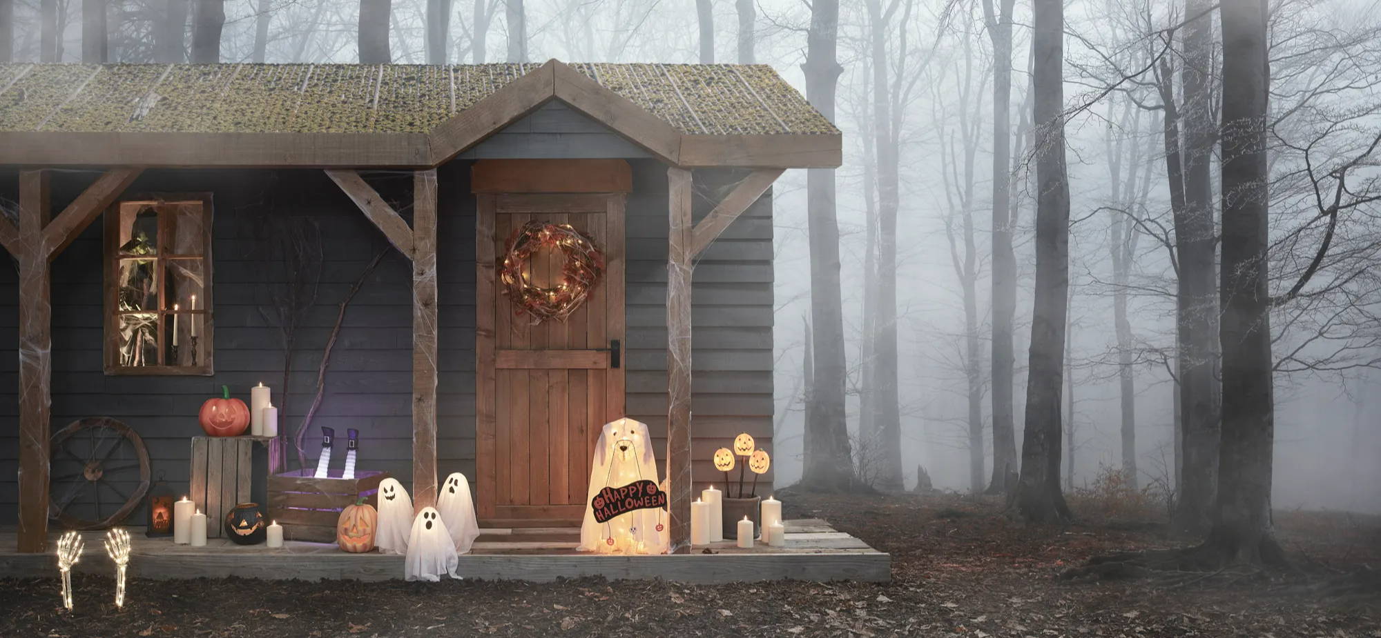 A spooky Halloween house setting in a forest with witches, ghost dogs, stake light and pumpkins.