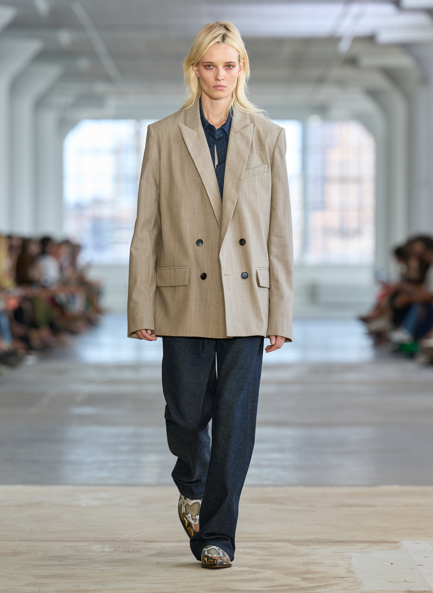 Model walking down runway in oversized suit jacket and dark pants.