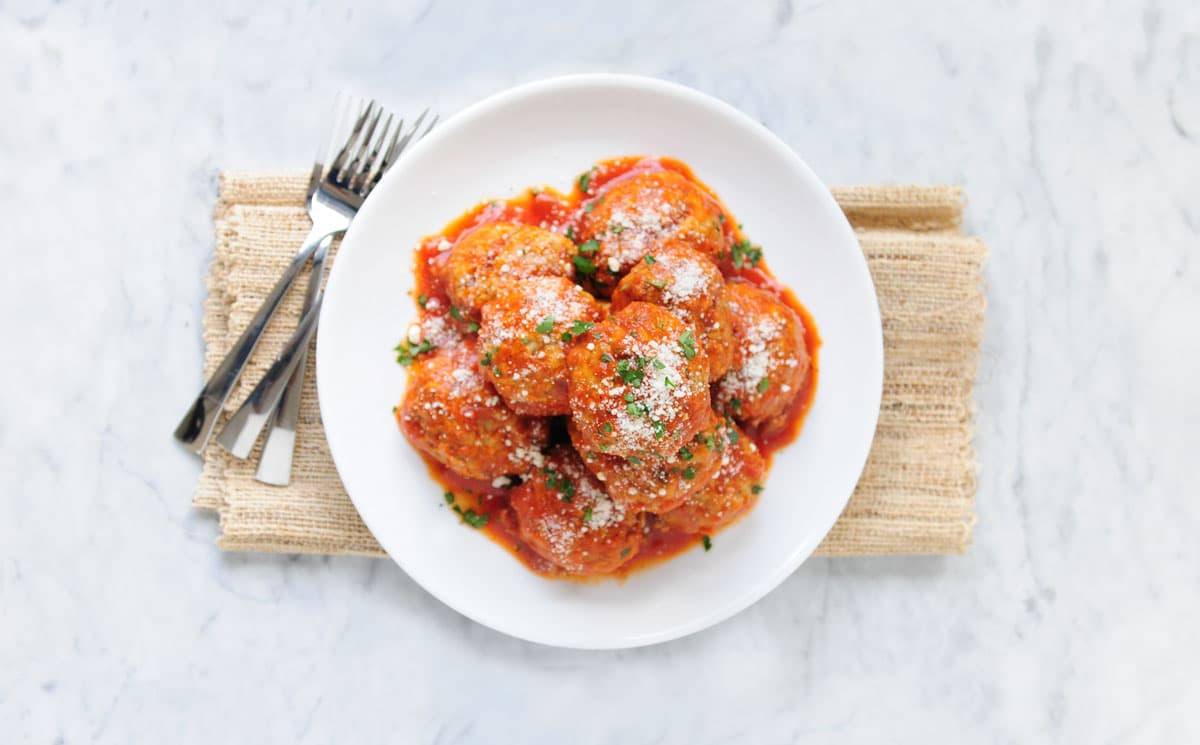 Downshot of meatballs with red sauce on white plate