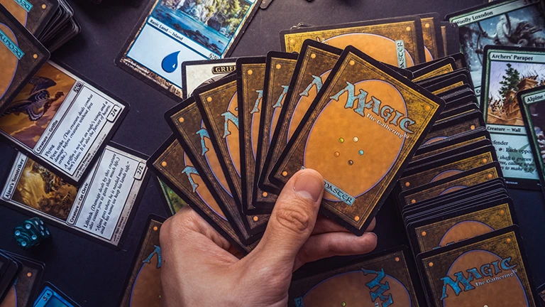 mtg double strike - A hand holding a fan of playing cards on a tabletop.