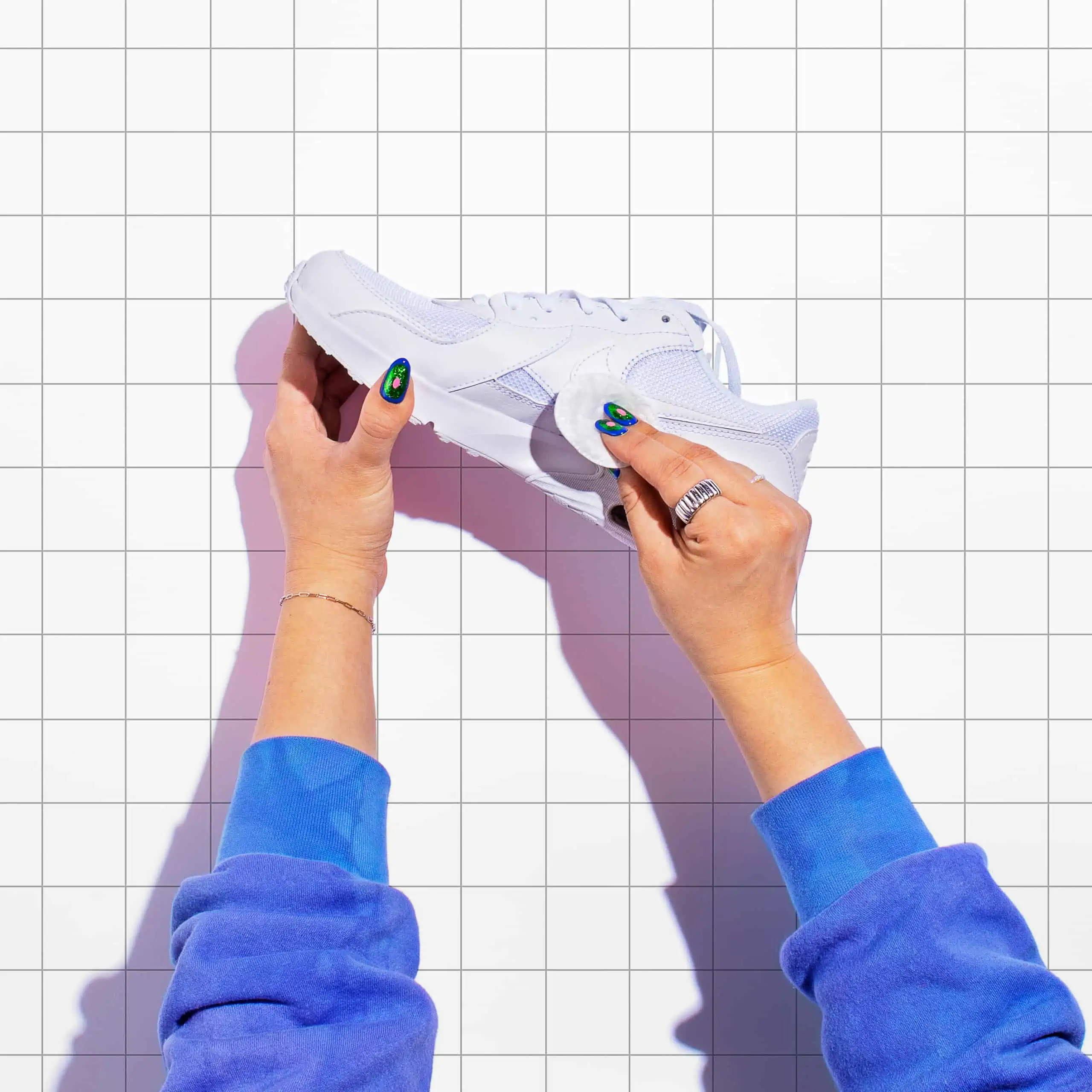 Hands holding a white sneaker against a grid background.