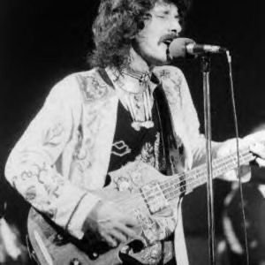 Musician singing into a microphone while playing an electric bass guitar.