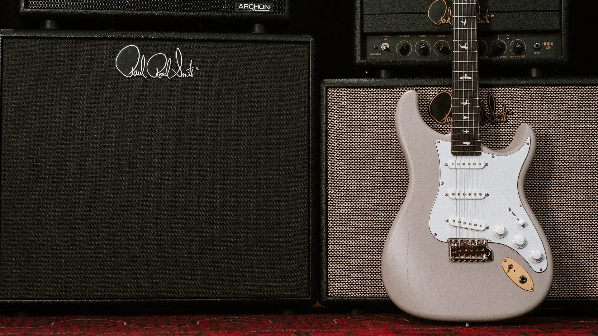 A PRS Silver Sky Dead Spec electric guitar next to amplifiers on a red carpet.