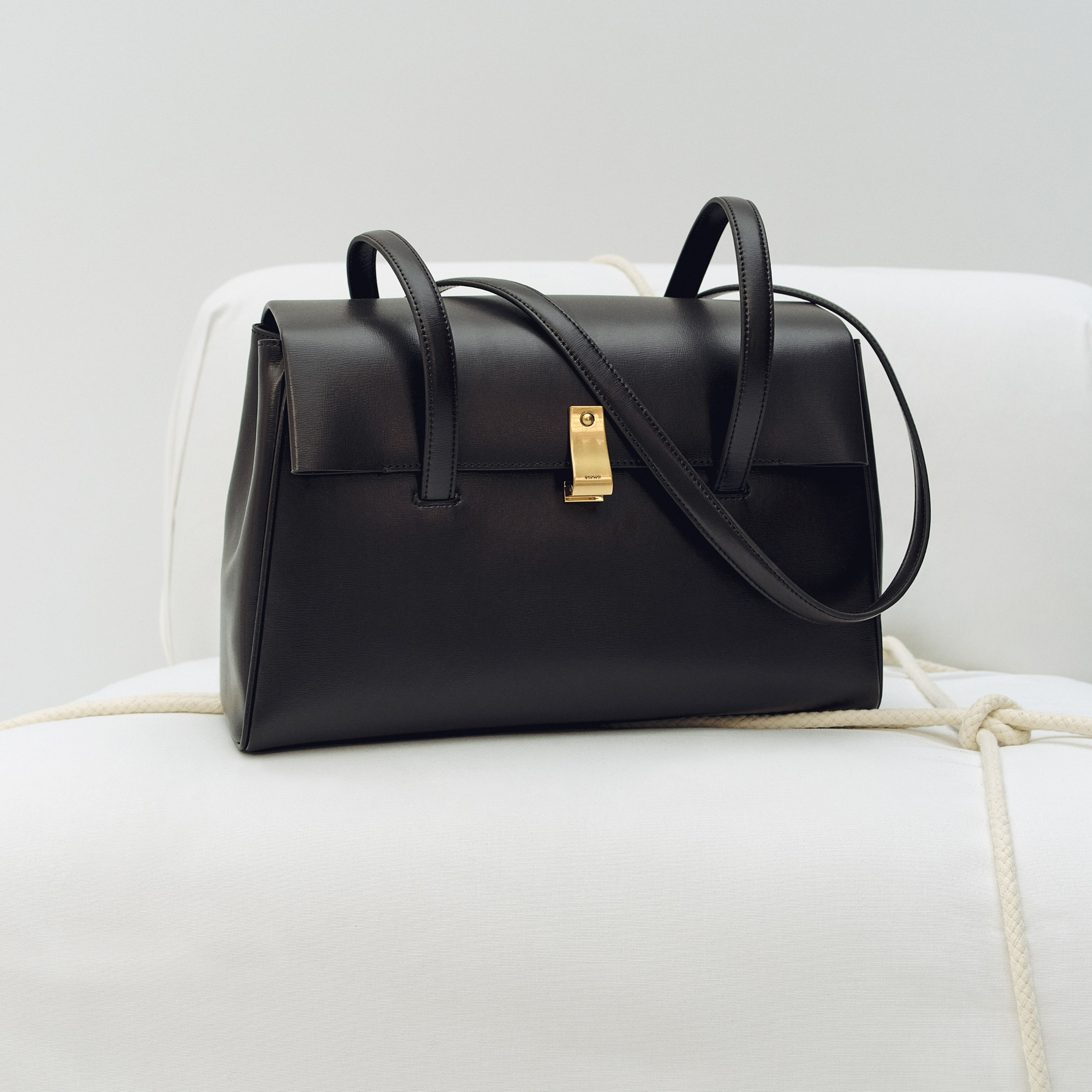 A stylish black handbag with a gold clasp on a white surface.