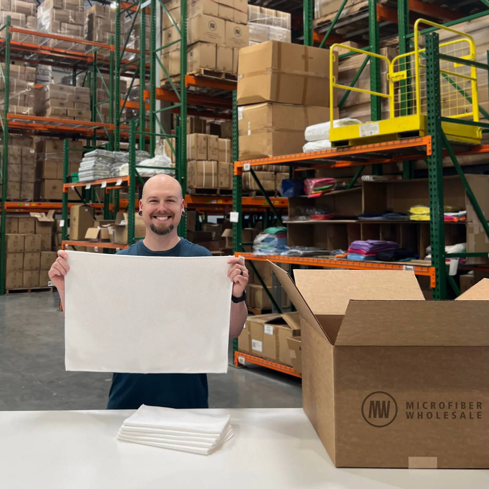 Man holding a sheet in a warehouse with stacked boxes in the background.