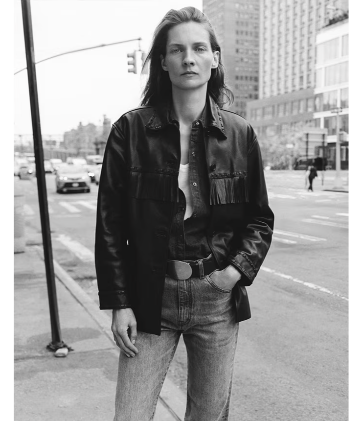 Person standing on a city street, wearing a black jacket and jeans.