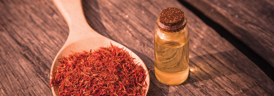 Saffron threads in a wooden spoon beside a small bottle of oil.