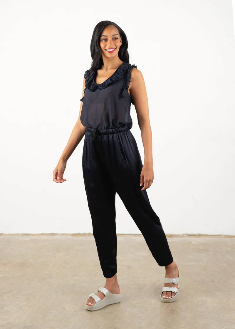 A model wearing a blue black sleeveless blouse with frill detailing around the neckline, blue black satin trousers and off white chunky platform slides