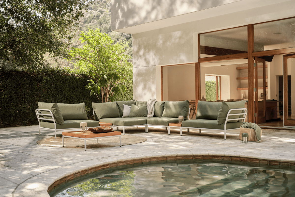 Modular outdoor sectional with green performance cushions and white metal frames arranged beside a pool in a modern backyard.