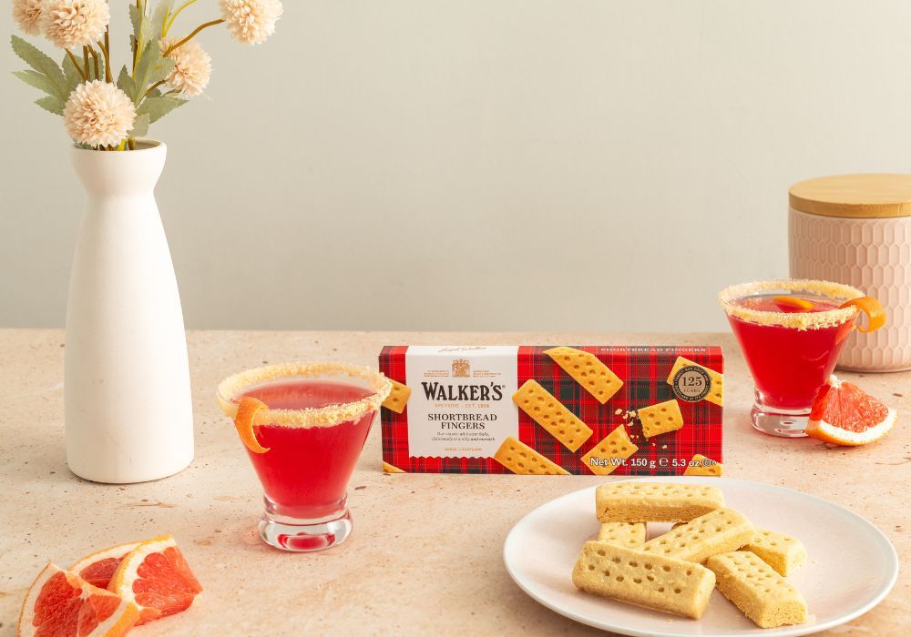 A table setting with drinks, cookies, and a vase of flowers.