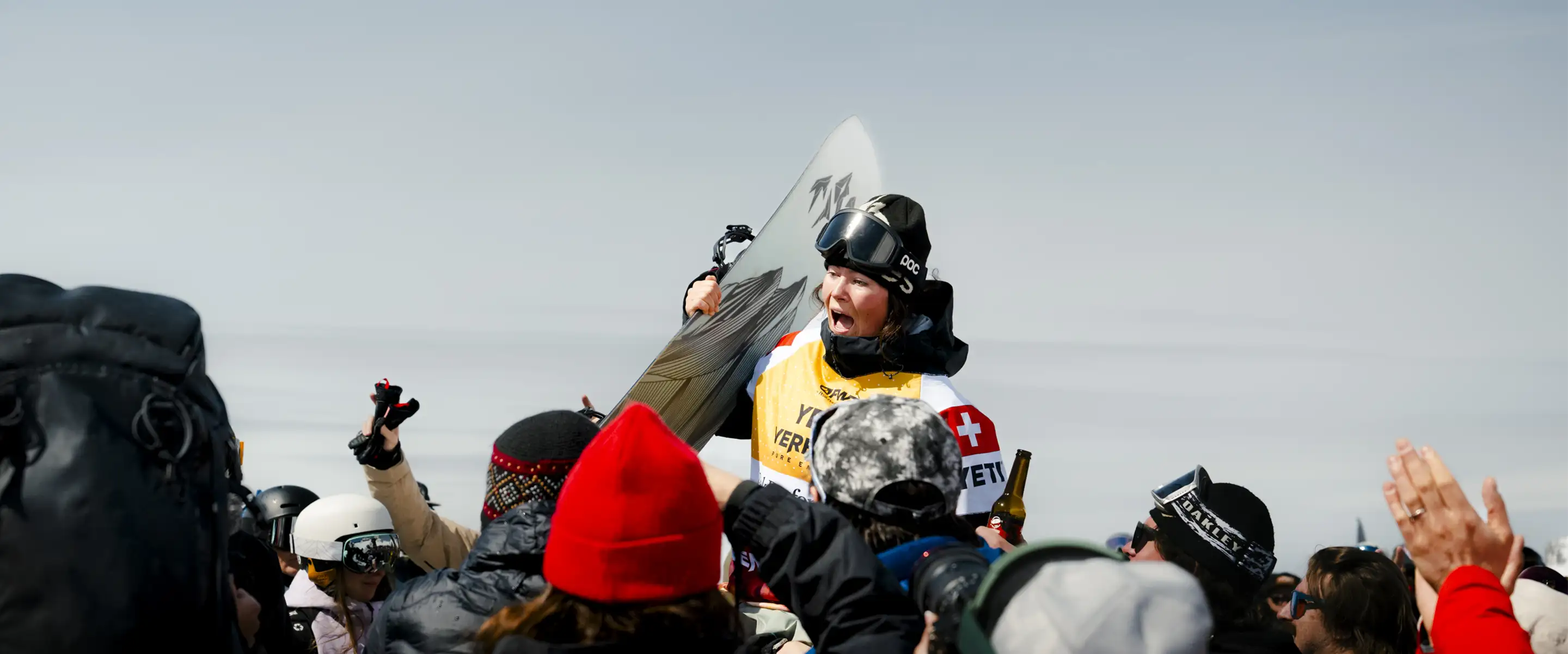Snowboarder celebrating with a crowd, holding a snowboard in victory.