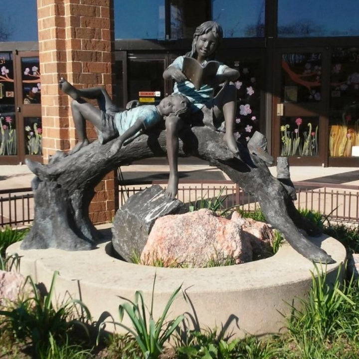 bronze statue of children reading  on a log