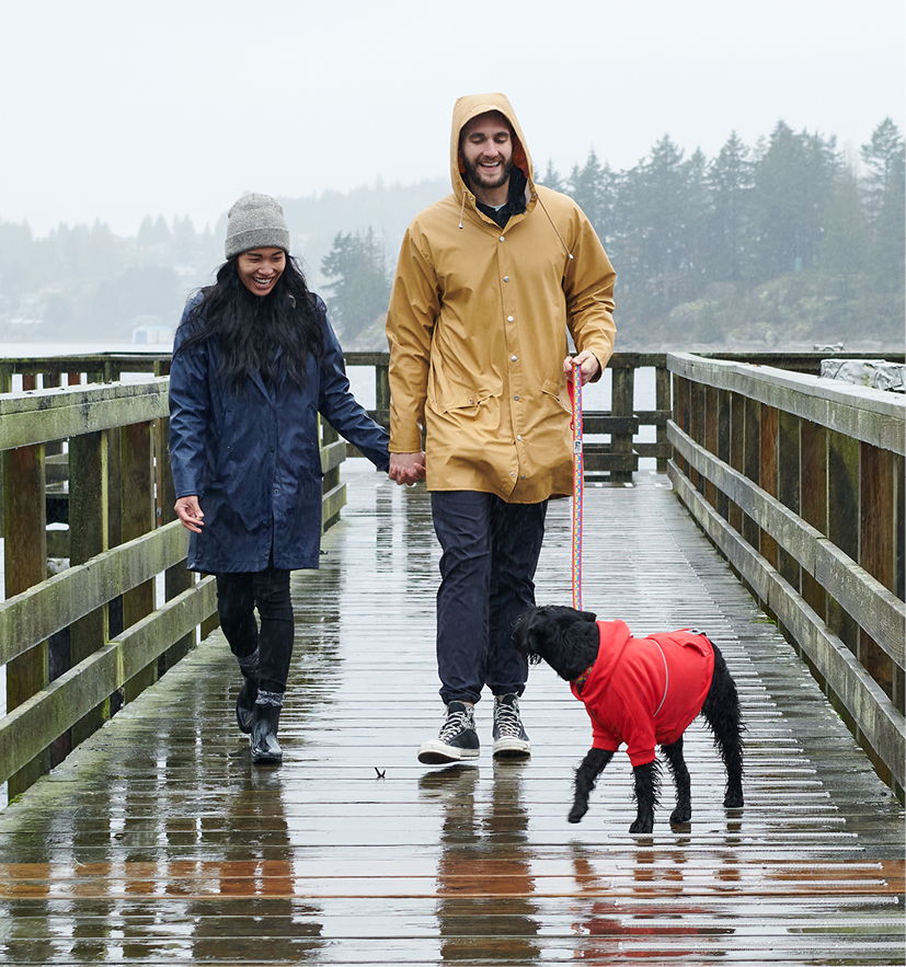 A couple walking a dog on a rainy boardwalk.