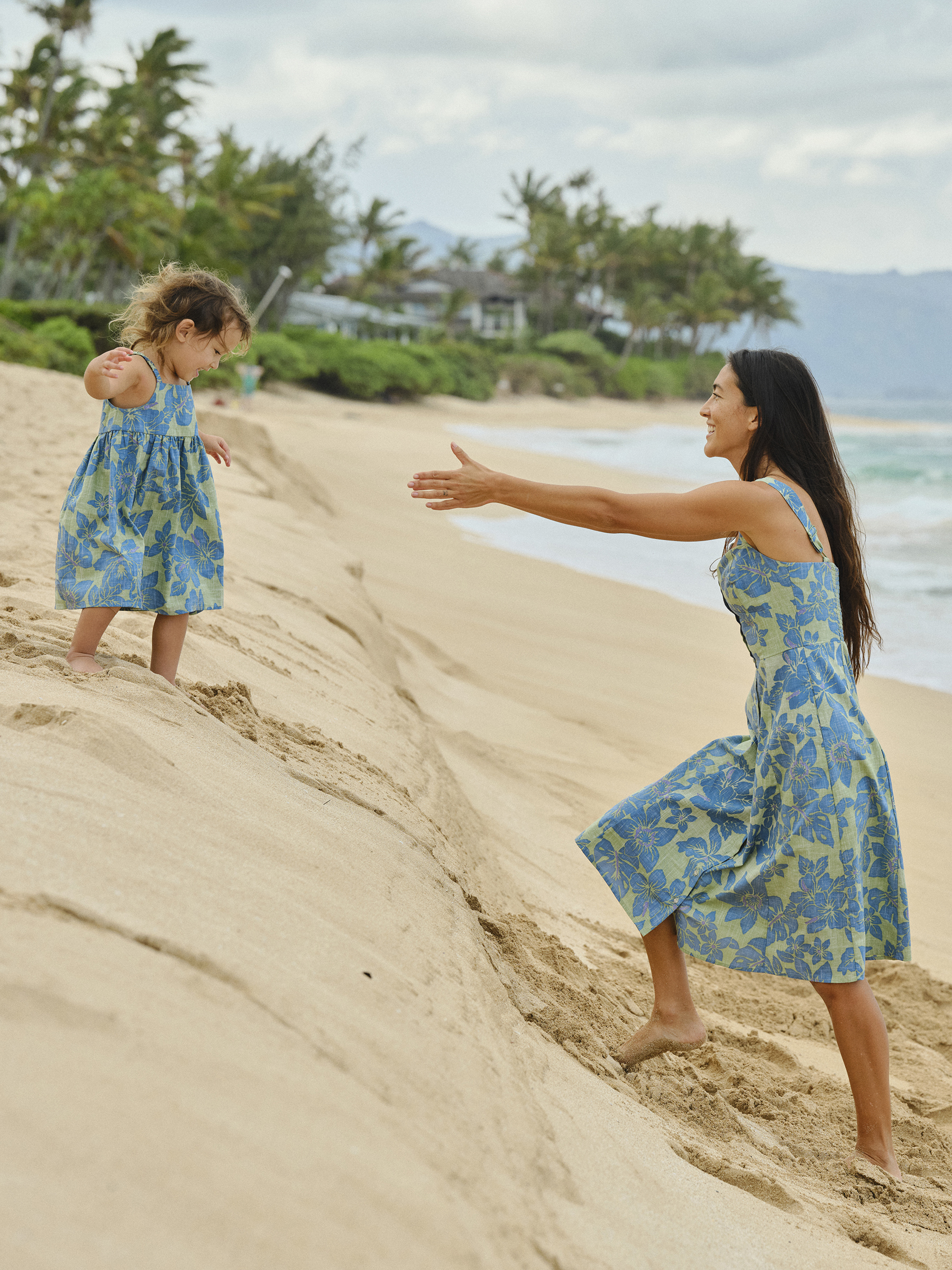 A woman reaching out to a child on a beach.