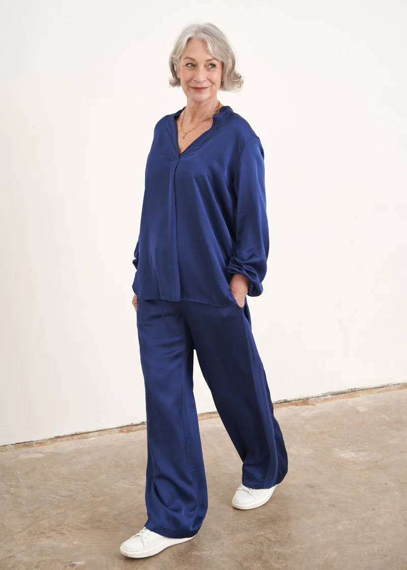 A model wearing a pair of blue satin wide leg trousers with a matching blouse