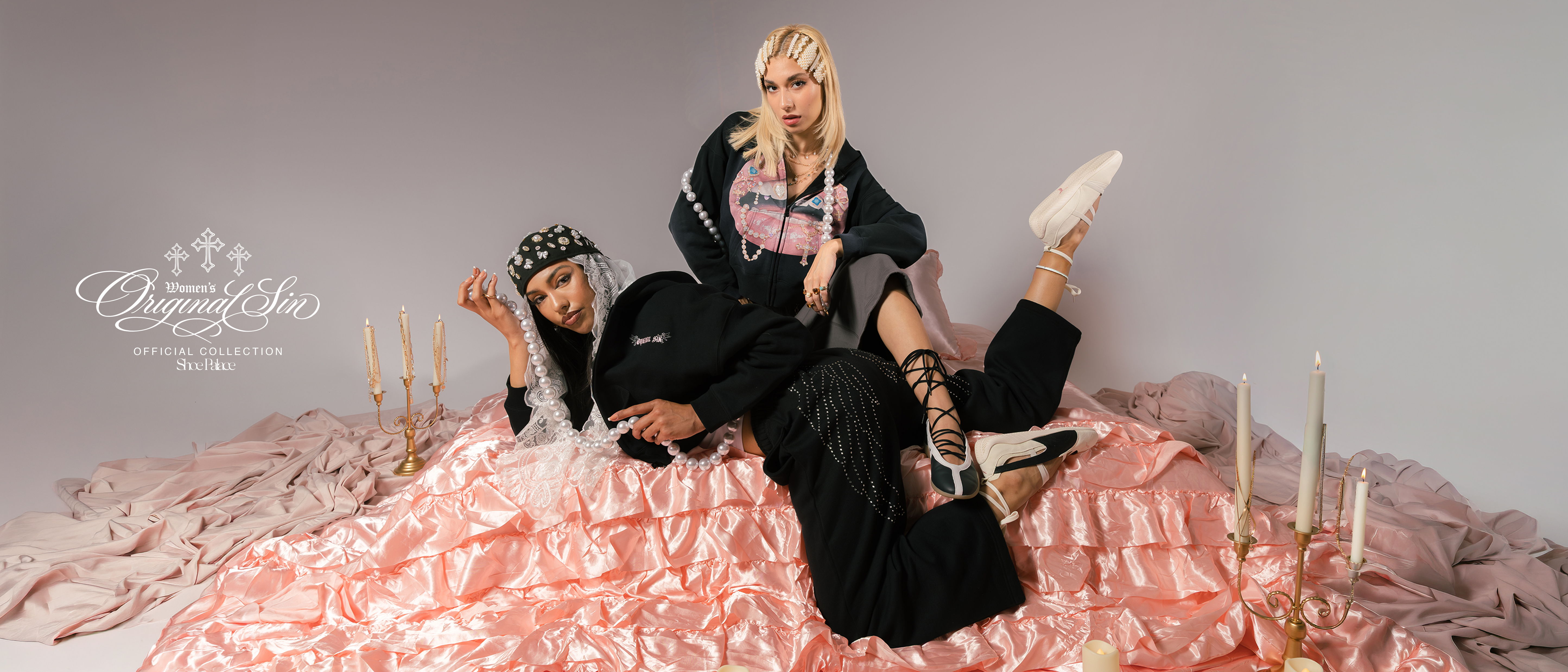 Two individuals in stylish outfits posed on a mound of pink material.