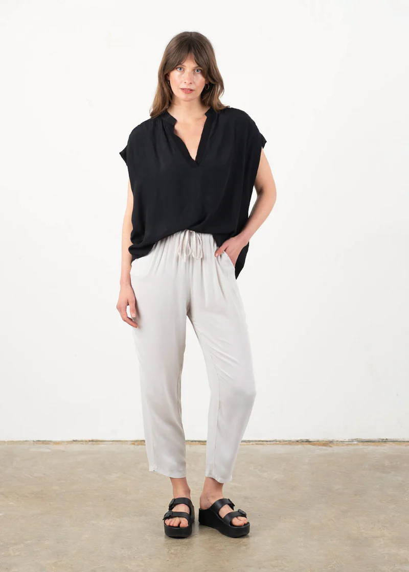 A model wearing an oversized, sleeveless black top with a v neckline with off white oatmeal linen trousers and black chunky platform slides