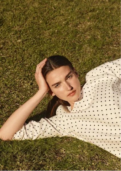 A woman lying on grass, wearing a polka dot shirt.