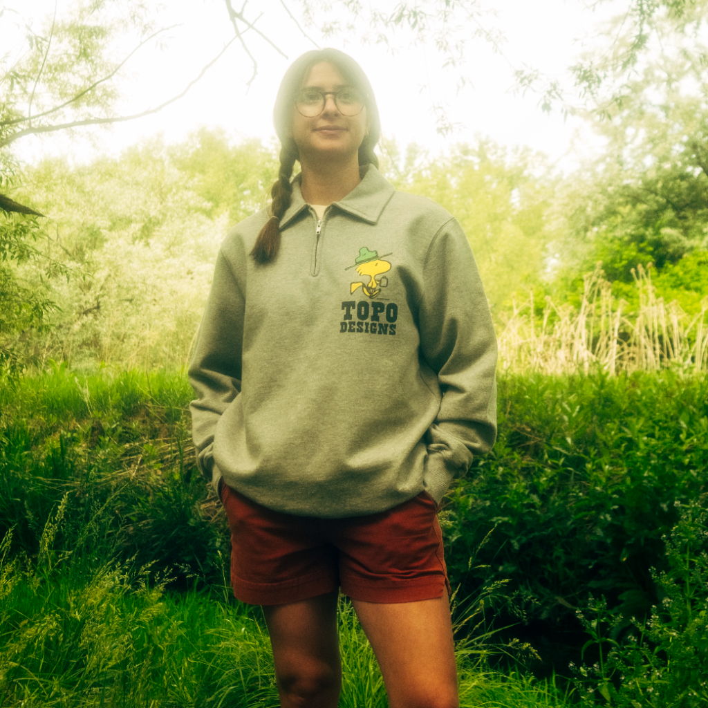 Person standing in nature, wearing a gray sweatshirt and orange shorts.