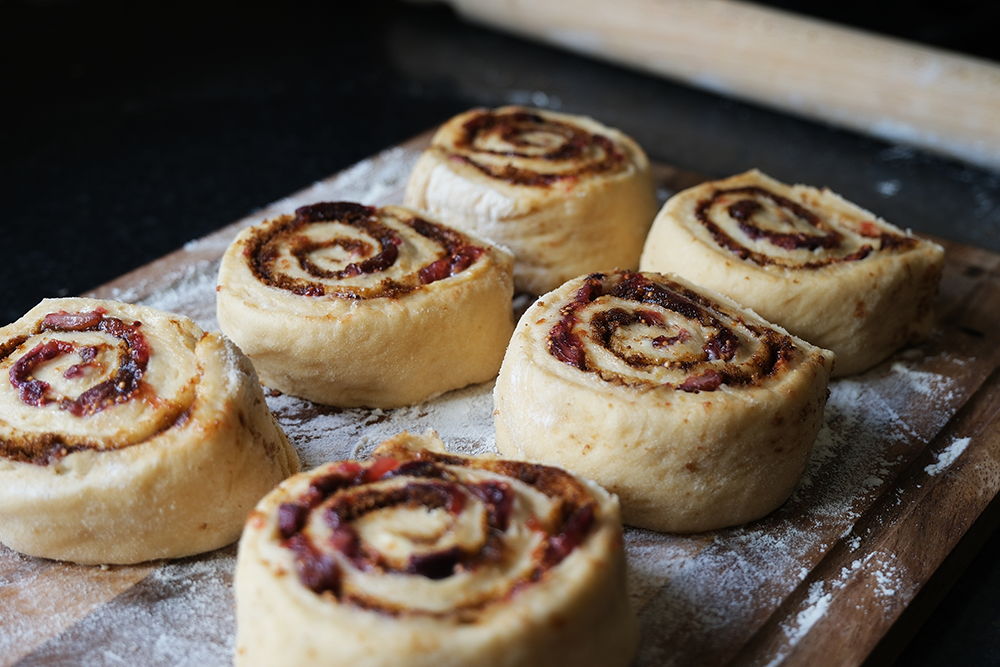 Freshly rolled cinnamon rolls on a wooden surface, ready for baking.