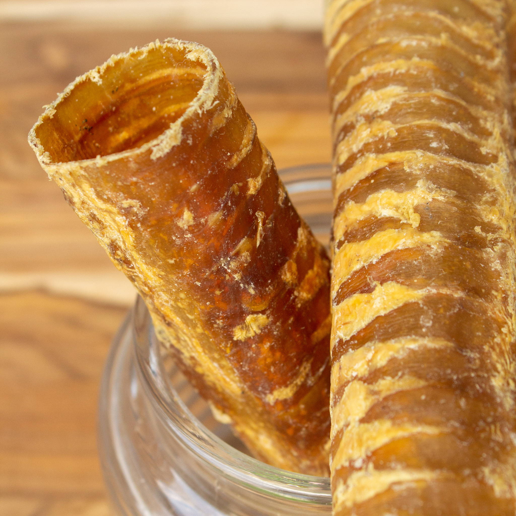 Close-up of two beef trachea chews in a glass jar on wooden surface.