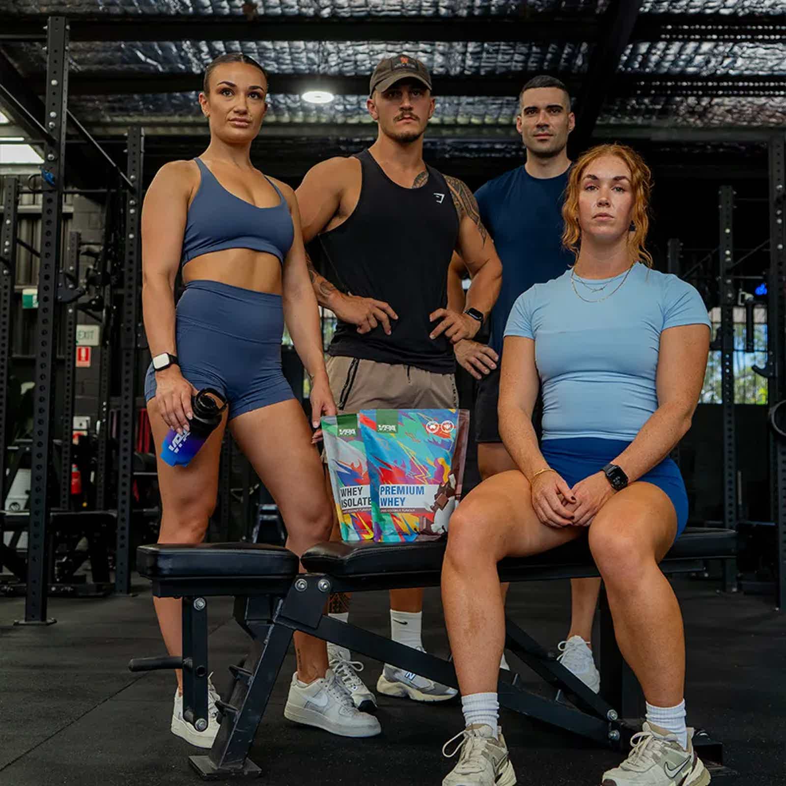 Four people posing together in a gym setting, wearing workout attire.