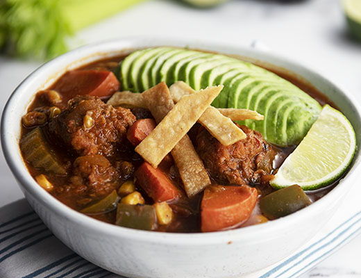Bowl of vegetarian meatball soup topped with lime, avocado, and tortilla strips.
