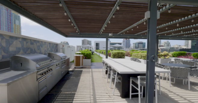 Rooftop patio with grill and dining area, city skyline in background.