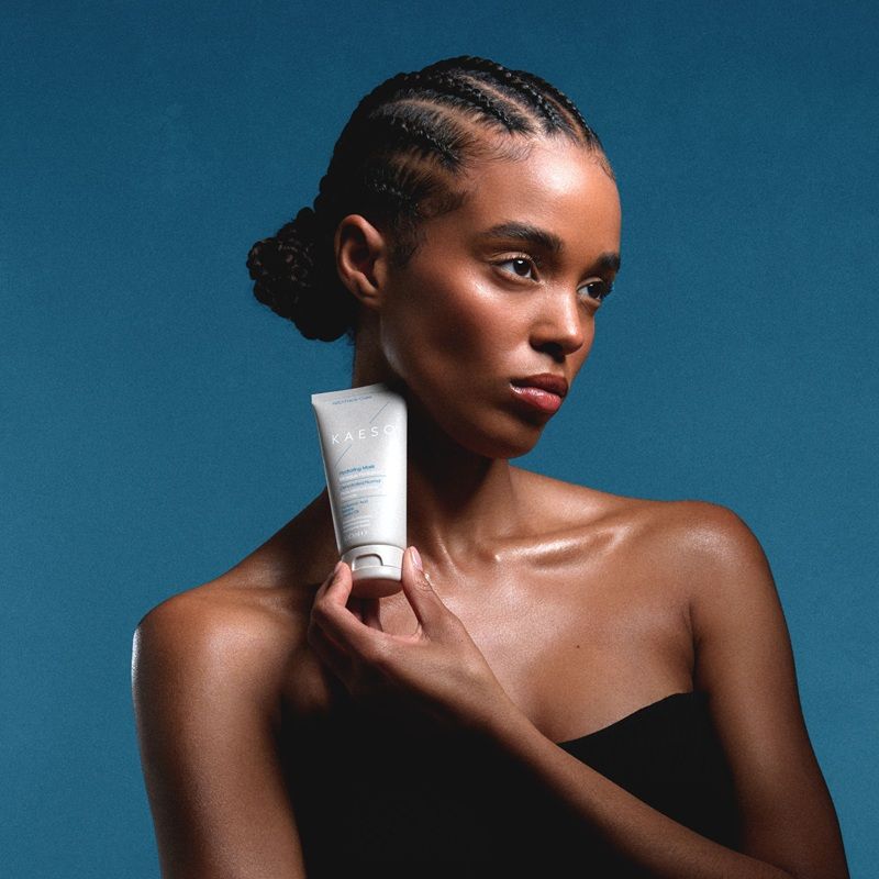 A woman holding a skincare product against a blue background.