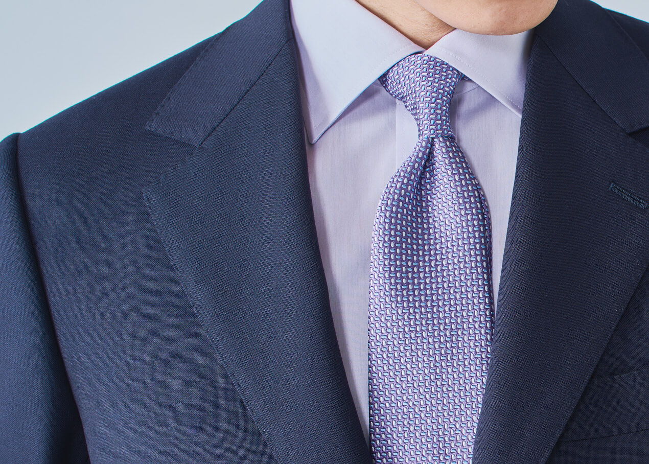A man in a suit with a light purple tie and shirt.