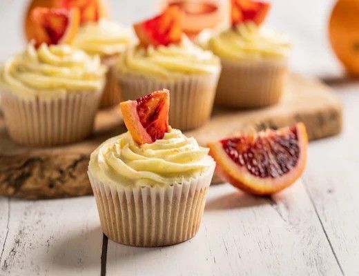 Cupcakes with cream frosting and blood orange slices on a wooden board.